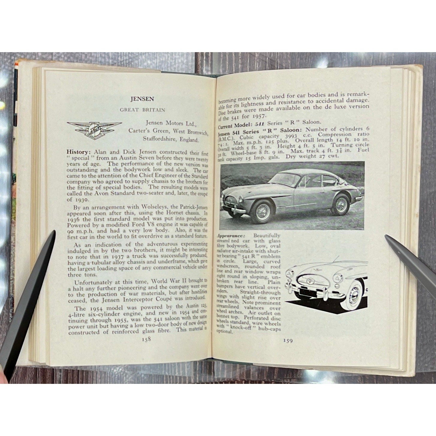 Open book with text and images of a vintage car on a metallic surface.